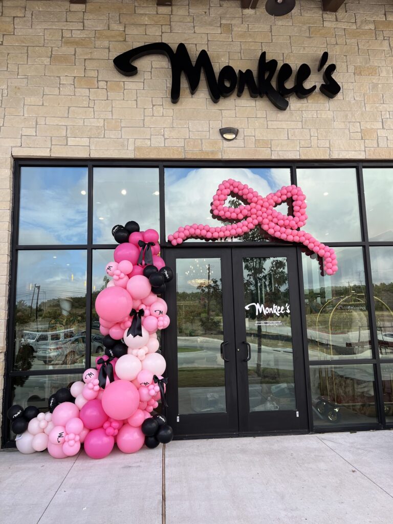 Oversized hot pink balloon bow and pink garland across a boutique storefront in Austin, TX