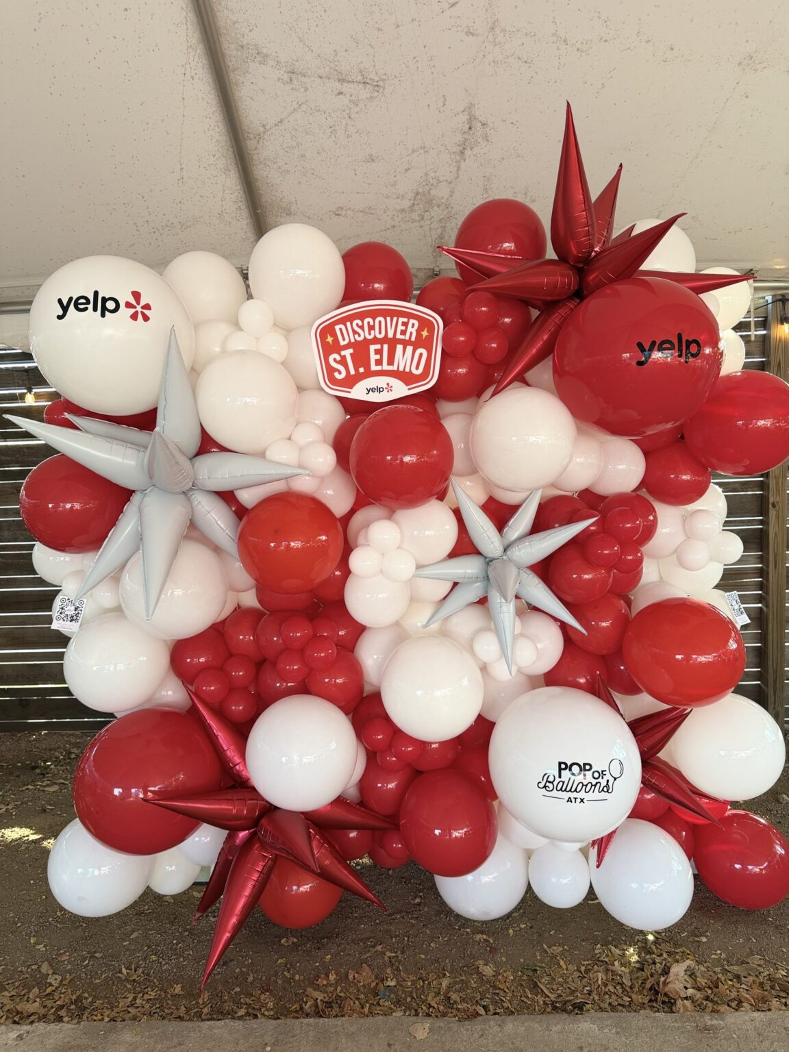 Red and white corporate balloon wall with silver starbursts and Yelp branding for a Discover St. Elmo event in Austin, TX