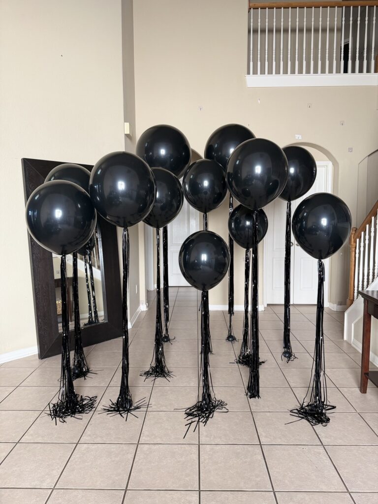 Row of oversized black helium balloons with long ribbon tails in a bright entryway in Austin, TX